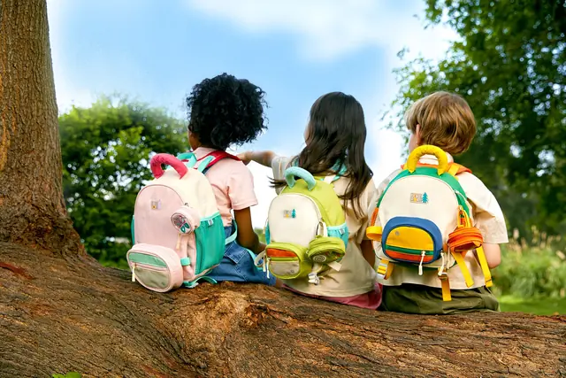 Children in mideer backpacks sitting on a tree, seen from behind